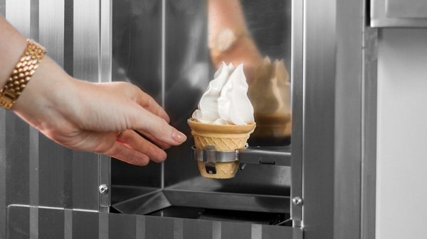 Hand reaching our for a soft ice cream from an ice cream machine