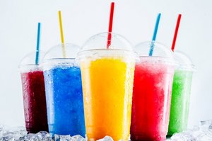 Five cups with straws and slush ice in different colours positioned on top of ice cubes